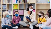 Pre-school teacher sits with students on floor of classroom