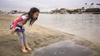 Girl looking into puddle on beach