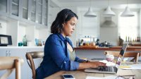 Woman at home sitting at table and writing on laptop.