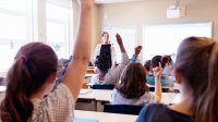 Middle school students raising hands in classroom