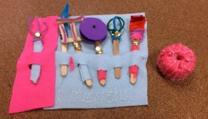 Six Pirate tool utensils make from popsicle sticks and pipe cleaners laid out in a row on a large piece of felt which can be rolled up