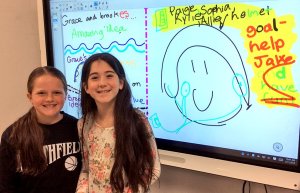 Two girls standing in front of an electronic whiteboard