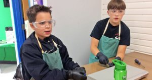 Two boys wearing safety goggles and green aprons
