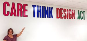 Woman standing in front of a wall under very large words: CARE THINK DESIGN ACT