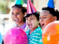 Three kids wearing party hats holding balloons