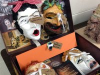 Four masks in the style of classical Greek theatre are displayed in an open box alongside images of Greek masks. 