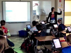 Teacher showing website items to very engaged students as they follow along on their tablets