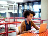 Girl sitting at a table next to stairs working on her laptop