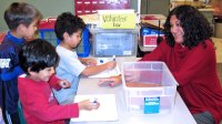 Teacher sitting at a table working with three young boys using markers