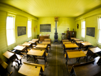 A fisheye photo of a classroom with wooden desks and a wood-burning stove.