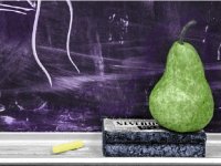 A photo of a pear on an eraser, on a chalkboard shelf.