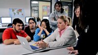 Teacher with students gathered around her looking at computer.