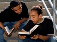 Two young men with open books in discussion