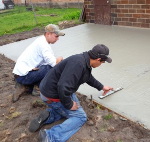 Two boys smoothing out a just-poured concrete slab next to the house