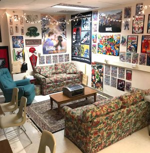 A classroom lounge area with hanging lights, movie posters, two couches, and a coffee table