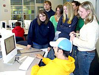 One student sitting in front of a computer as six stand around him listening