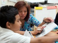 Teacher helping a boy read pointing to words in a book