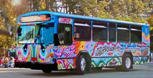 An exterior shot of a tie-dye painted bus parked on the street with eyes painted on the front and 'Art' painted on the side. 
