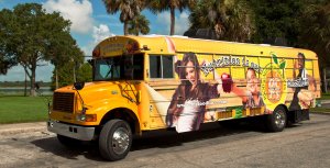 Nutrition is our mission is painted on a bus that's parked on the street. A picture of a teen girl with her arms raised in celebration, a young boy holding an apple, and a teen boy holding a sandwich are painted on the bus, as well.