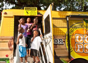 Five students are smiling, exiting the stairway of a bus that says, 'Food and Nutrition' on the side.