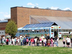 Students line up beside a blue bus with a glass roof.