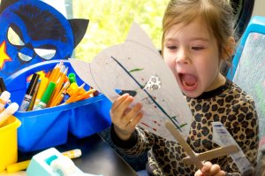 A young girl is staring excitedly at a paper mask she made on an art bus. 