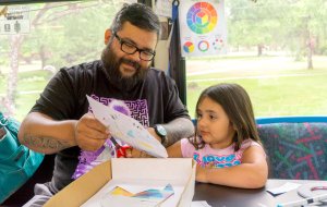 A father and daughter are making art on a bus with paper and markers.