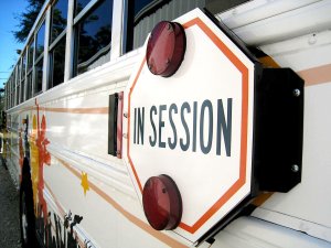 An exterior side shot of a bus. The stop sign says, 'In Session,' instead of 'Stop.'