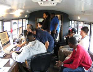 Teens and adults are sitting in a bus editing music on computers. 