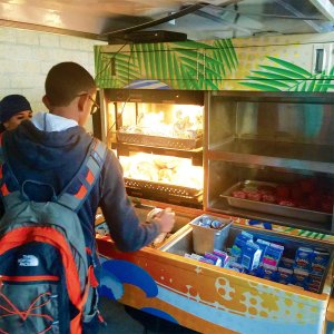 A student is reaching into the back of a golf cart filled with boxed milk, fruit cups, and wrapped hot foods.