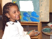 Young girl in smock in front of an easel with paint on her hands