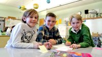 Three boys sitting together at a table in class smiling at the camera