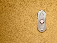 A closeup of a doorbell against a tan, textured wall. 