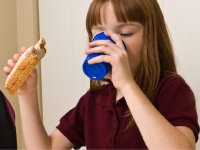 Young girl drinking with one hand and holding a peanut butter sandwich in the other