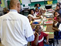 Teacher wearing a shirt that says "Stir The Soul" standing in front of class reading to captivated students