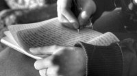 Close-up black-and-white photo of a student’s hands as they write in a journal.