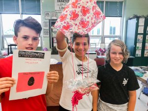 Three students holding up a parachute project they built