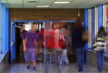 High school students are walking through one school hallway into another through opened double doors. The students are blurred as to imply fast movement and the passing of time.