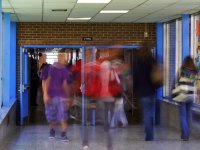 High school students are walking through one school hallway into another through opened double doors. The students are blurred as to imply fast movement and the passing of time.