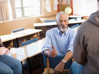 Man sitting in a chair talkling to two other people.