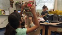 Two students test the fit of a suit of cardboard armor.