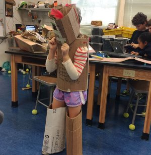 A girl poses in cardboard armor in a makerspace.