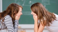 Two smiling girls stare into each other’s eyes in class.