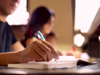 A photo of the arm and hand of a high school male, writing in his notebook.