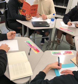 A group of high school students reading poems and writing notes in a circle of desks