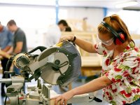 Girl operating a large table saw wearing safety headphones and goggles