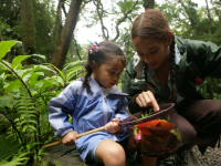 Older girl pointing at something in a net held by a younger girl in a forest