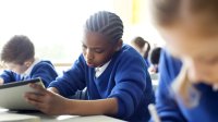 Students in uniform sweaters sit in a classroom and write by hand.