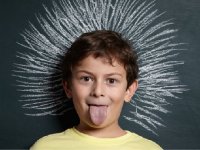 Boy with tongue out standing in front of chalk board drawing of big hair sticking up