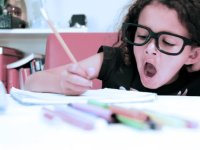 Young girl with glasses writing in a binder and yawning